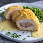 chicken cordon bleu with sauce and peas on plate