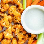 air fryer cauliflower wings on circular white plate with celery and carrot sticks and dipping sauce.