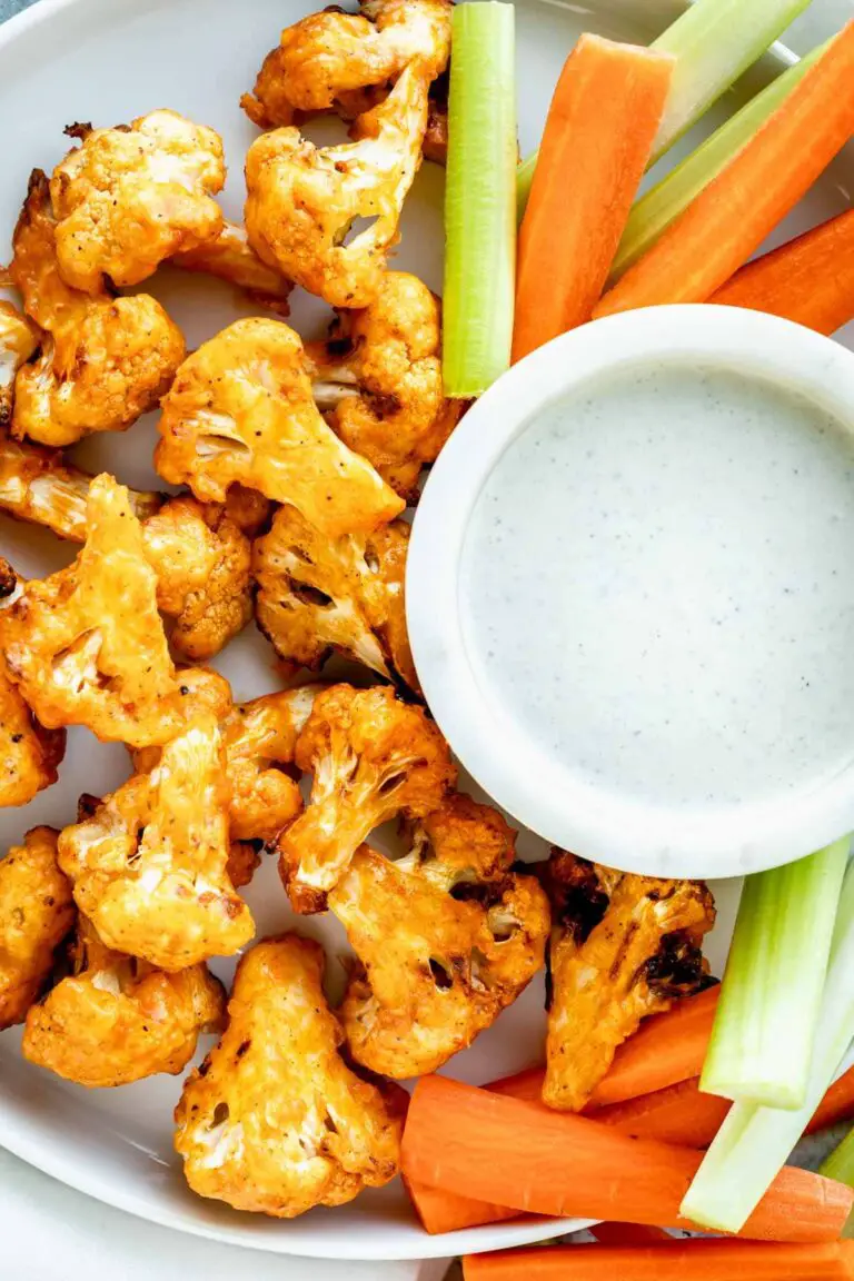 air fryer cauliflower wings on circular white plate with celery and carrot sticks and dipping sauce.