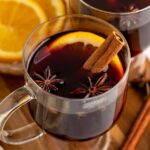 mugs of mulled wine with cinnamon sticks, orange slices and spices.