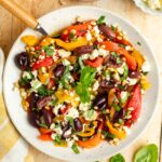 roasted pepper salad in white bowl with basil, pine nuts, olives, and feta cheese.